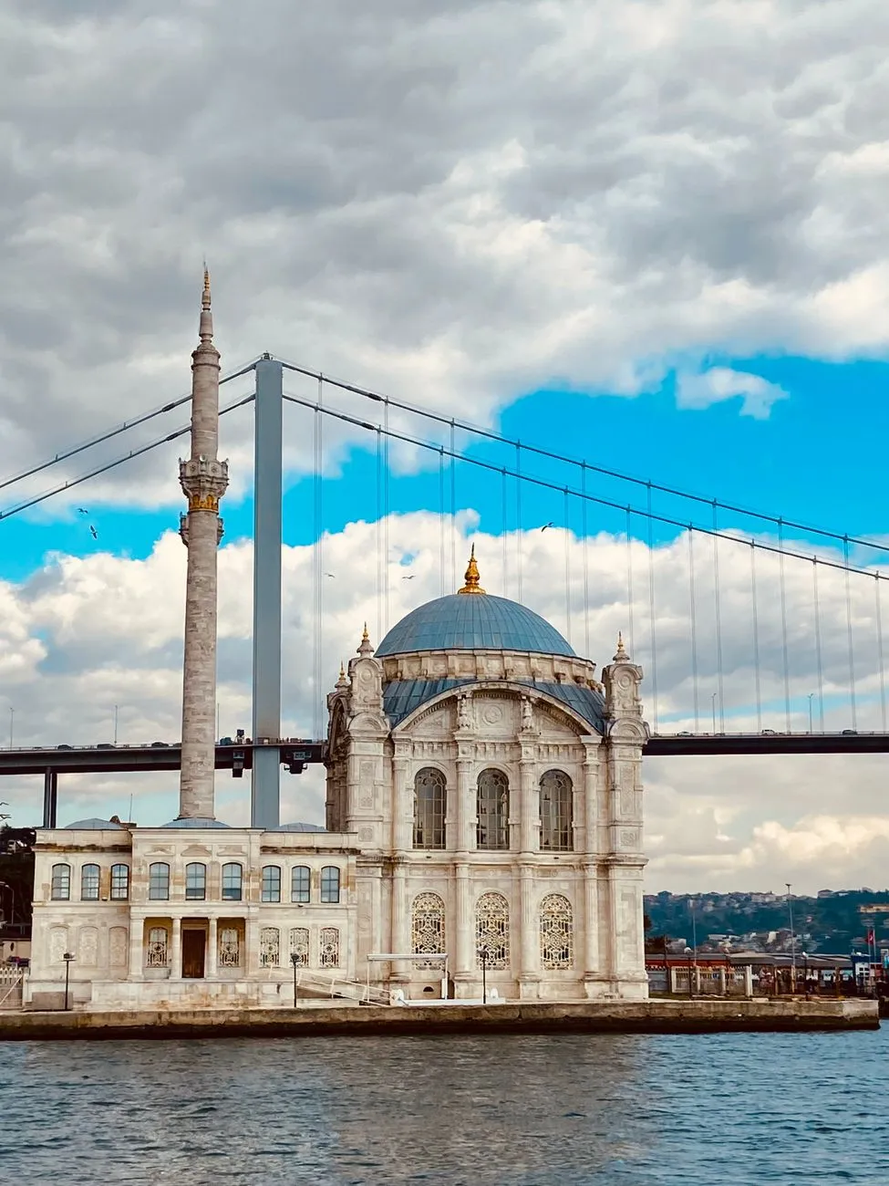 Ortaköy Mosque with the Bosphorus Bridge in Istanbul under a cloudy sky.