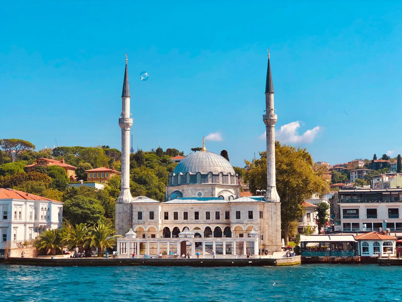 Charming view of a mosque by the waterfront in Istanbul during summer, showcasing its minarets and vibrant surroundings.
